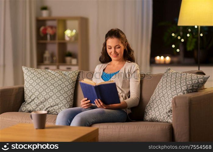 leisure, literature and people concept - young woman reading book at home in evening. young woman reading book at home in evening
