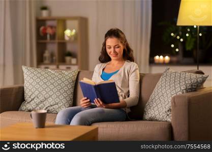 leisure, literature and people concept - young woman reading book at home in evening. young woman reading book at home in evening