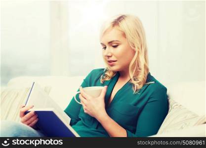 leisure, literature and people concept - young woman with tea cup reading book at home. young woman with tea cup reading book at home