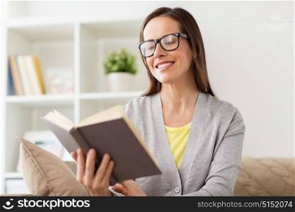 leisure, literature, education and people concept - young woman in glasses reading book at home. young woman in glasses reading book at home