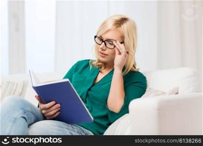 leisure, literature, education and people concept - young woman in glasses reading book at home