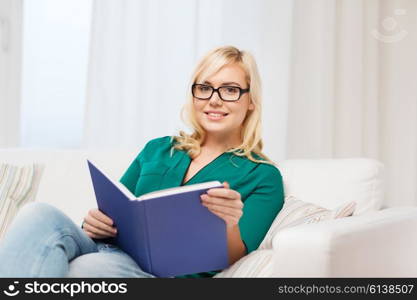 leisure, literature, education and people concept - young woman in glasses reading book at home