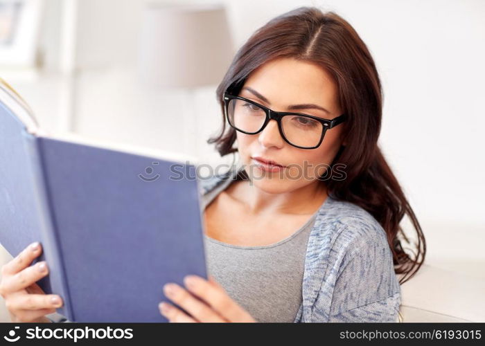 leisure, literature, education and people concept - young woman in glasses reading book at home