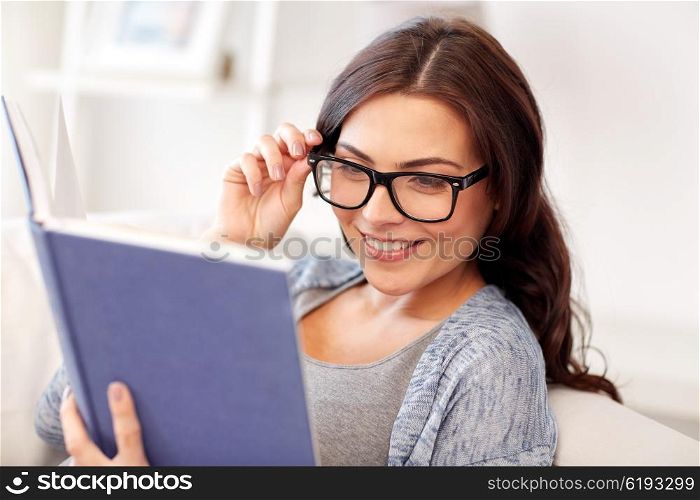 leisure, literature, education and people concept - young woman in glasses reading book at home