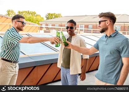leisure, male friendship and people concept - happy men or friends drinking beer and clinking bottles at rooftop party in summer. happy male friends drinking beer at rooftop party