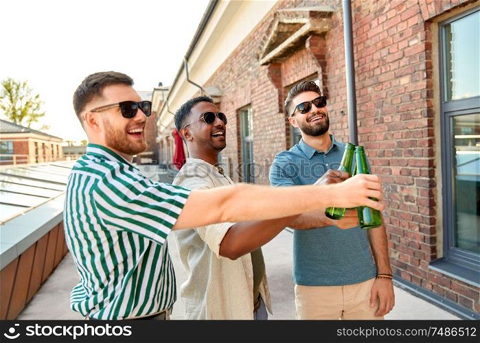 leisure, male friendship and people concept - happy men or friends drinking beer and clinking bottles at rooftop party in summer. happy male friends drinking beer at rooftop party