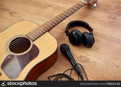 leisure, music and musical instruments concept - close up of acoustic guitar, microphone and headphones on black table. close up of guitar, microphone and headphones