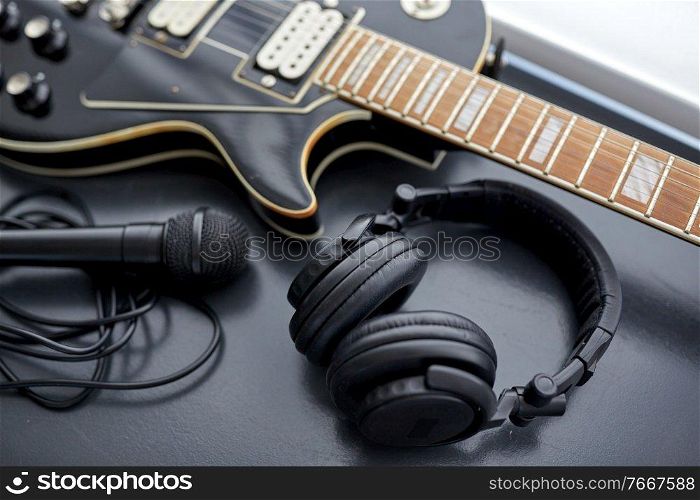 leisure, music and musical instruments concept - close up of bass guitar, microphone and headphones on black table. close up of bass guitar, microphone and headphones