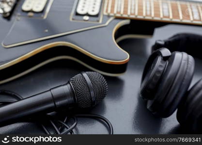 leisure, music and musical instruments concept - close up of bass guitar, microphone and headphones on black table. close up of bass guitar, microphone and headphones