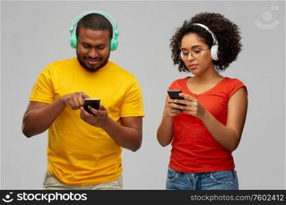 leisure, music and people concept - african american couple with headphones and smartphones over grey background. african couple with headphones and smartphones
