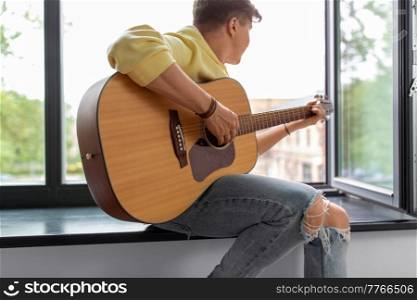 leisure, music and people concept - close up of man playing guitar sitting on windowsill. close up of man playing guitar sitting on sill