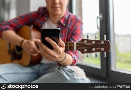 leisure, music and people concept - close up of man with guitar and smartphone sitting on windowsill. man with guitar and phone sitting on sill