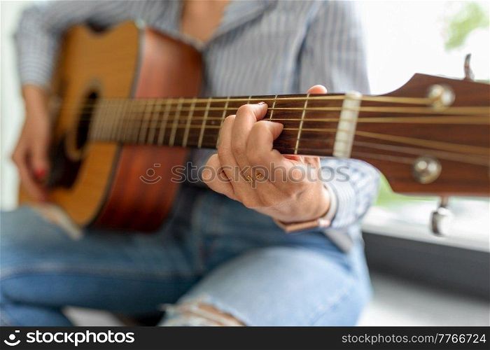 leisure, music and people concept - close up of woman playing guitar sitting on windowsill. close up of woman playing guitar sitting on sill