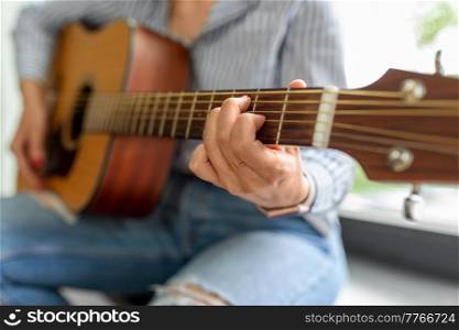 leisure, music and people concept - close up of woman playing guitar sitting on windowsill. close up of woman playing guitar sitting on sill