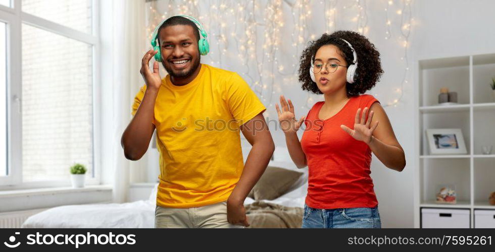 leisure, music and people concept - happy african american couple with headphones dancing over home bedroom background. african american couple with headphones dancing