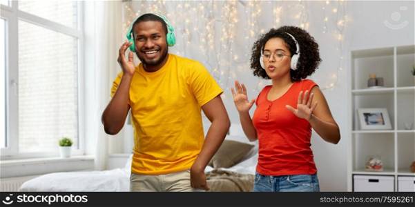 leisure, music and people concept - happy african american couple with headphones dancing over home bedroom background. african american couple with headphones dancing