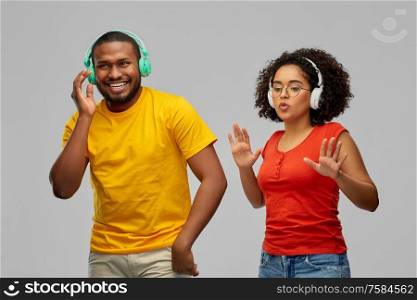 leisure, music and people concept - happy african american couple with headphones dancing over grey background. african american couple with headphones dancing