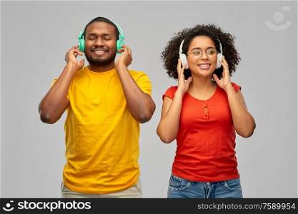 leisure, music and people concept - happy smiling african american couple with headphones over grey background. happy african american couple with headphones