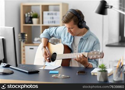 leisure, music and people concept - young man or musician in headphones playing guitar sitting at table at home. man in headphones playing guitar at home