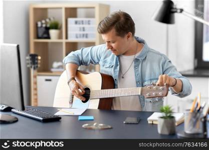 leisure, music and people concept - young man or musician playing guitar sitting at table at home. young man playing guitar sitting at table at home