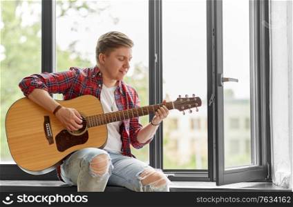 leisure, music and people concept - young man or musician playing guitar sitting on windowsill. young man playing guitar sitting on windowsill