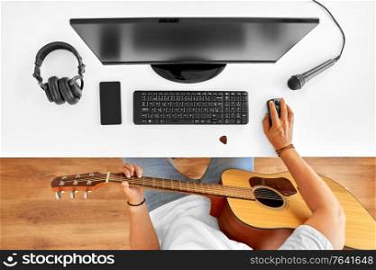 leisure, music and people concept - young man or musician with computer and guitar sitting at table. young man with computer and guitar at table