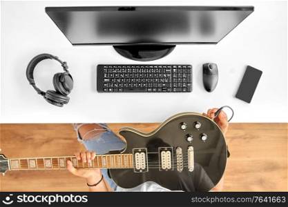 leisure, music and people concept - young man or musician with computer tuning guitar sitting at table. young man with computer tuning guitar at table