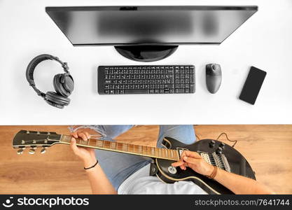 leisure, music and people concept - young man or musician with computer playing guitar sitting at table. young man with computer playing guitar at table