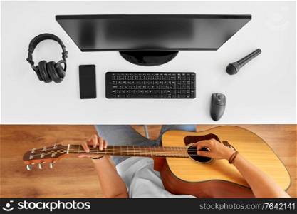 leisure, music and people concept - young man or musician with computer playing guitar sitting at table. young man with computer playing guitar at table