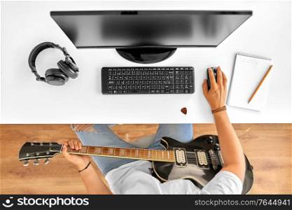 leisure, music and people concept - young man or musician with computer and guitar sitting at table. young man with computer and guitar at table