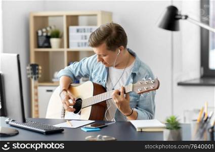 leisure, music and people concept - young man or musician with earphones and smartphone playing guitar at home. man with earphones and smartphone playing guitar