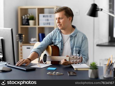 leisure, music and people concept - young man or musician with guitar and computer sitting at table at home. young man with guitar and computer at home