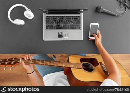 leisure, music and people concept - young man or musician with guitar, smartphone and laptop computer sitting at table. young man with guitar and smartphone at table