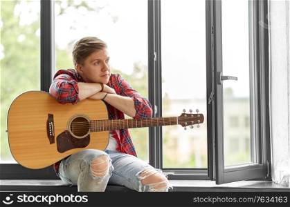 leisure, music and people concept - young man or musician with guitar sitting on windowsill. young man with guitar sitting on windowsill