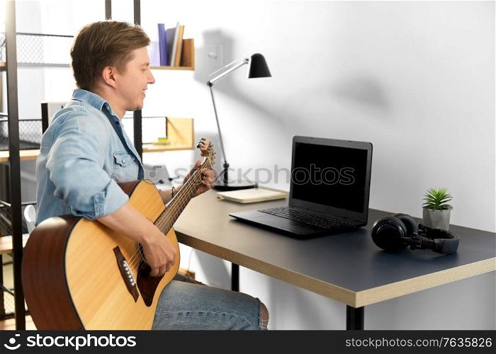 leisure, music and people concept - young man or musician with laptop computer and guitar sitting at table at home. young man with laptop and guitar at home