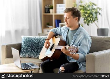 leisure, music and people concept - young man or musician with laptop computer playing guitar at home. young man with laptop playing guitar at home