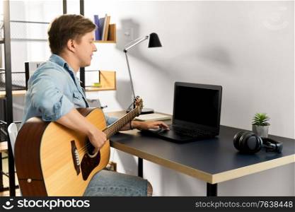 leisure, music and people concept - young man or musician with laptop computer and guitar sitting at table at home. young man with laptop and guitar at home