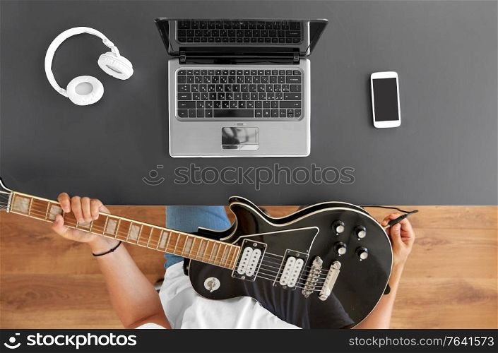 leisure, music and people concept - young man or musician with laptop computer tuning guitar sitting at table. young man with laptop tuning guitar at table