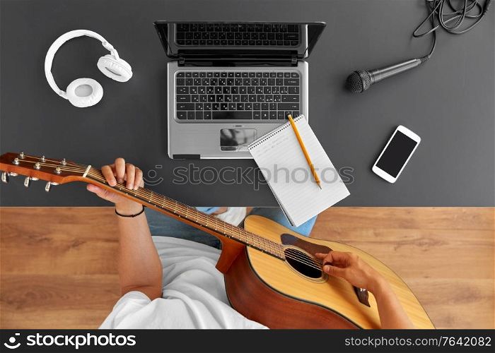 leisure, music and people concept - young man or musician with laptop computer playing guitar sitting at table. young man with laptop playing guitar at table