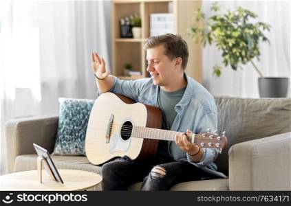 leisure, music and people concept - young man or musician with tablet pc computer and guitar having video call at home. man with tablet pc and guitar having video call