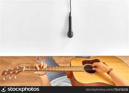 leisure, music and people concept - young man with microphone on white table playing guitar. man with microphone on table playing guitar