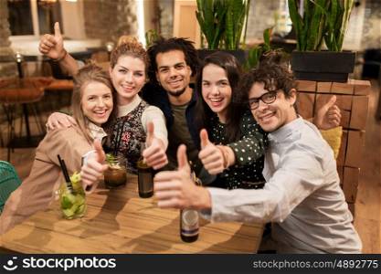 leisure, party, people and holidays concept - happy friends with drinks showing thumbs up at bar or cafe
