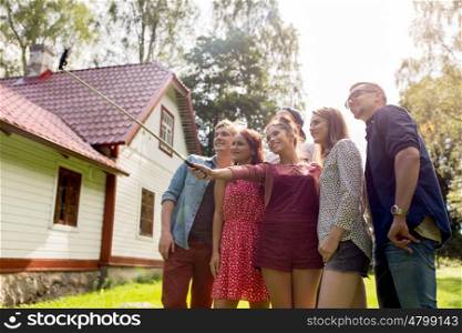 leisure, party, technology, people and holidays concept - happy friends taking picture with smartphone selfie stick at summer garden