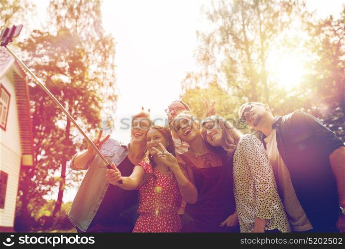 leisure, party, technology, people and holidays concept - happy friends taking picture with smartphone selfie stick at summer garden. friends taking selfie at party in summer garden
