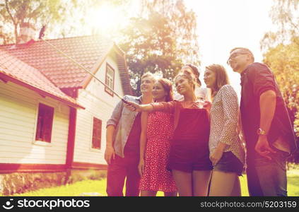 leisure, party, technology, people and holidays concept - happy friends taking picture with smartphone selfie stick at summer garden. friends taking selfie at party in summer garden