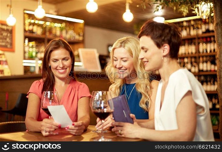 leisure, payment and lifestyle concept - happy women with bill and wallet at restaurant or wine bar. women looking at bill at wine bar or restaurant