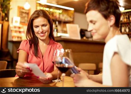leisure, payment and lifestyle concept - happy women with bill and wallet at restaurant or wine bar. women looking at bill at wine bar or restaurant