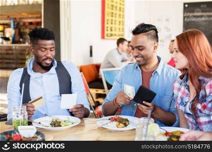leisure, payment and people concept - happy friends with money and credit card paying bill for food at restaurant. happy friends paying bill for food at restaurant