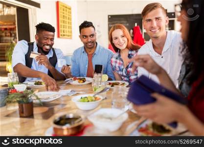 leisure, payment and people concept - happy friends with money and credit card paying bill for food at restaurant. happy friends with money paying bill at restaurant