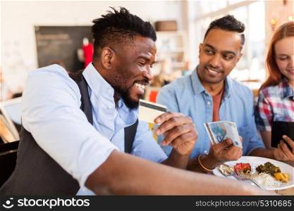leisure, payment and people concept - happy friends with money and credit card paying bill for food at restaurant. happy friends with money paying bill at restaurant